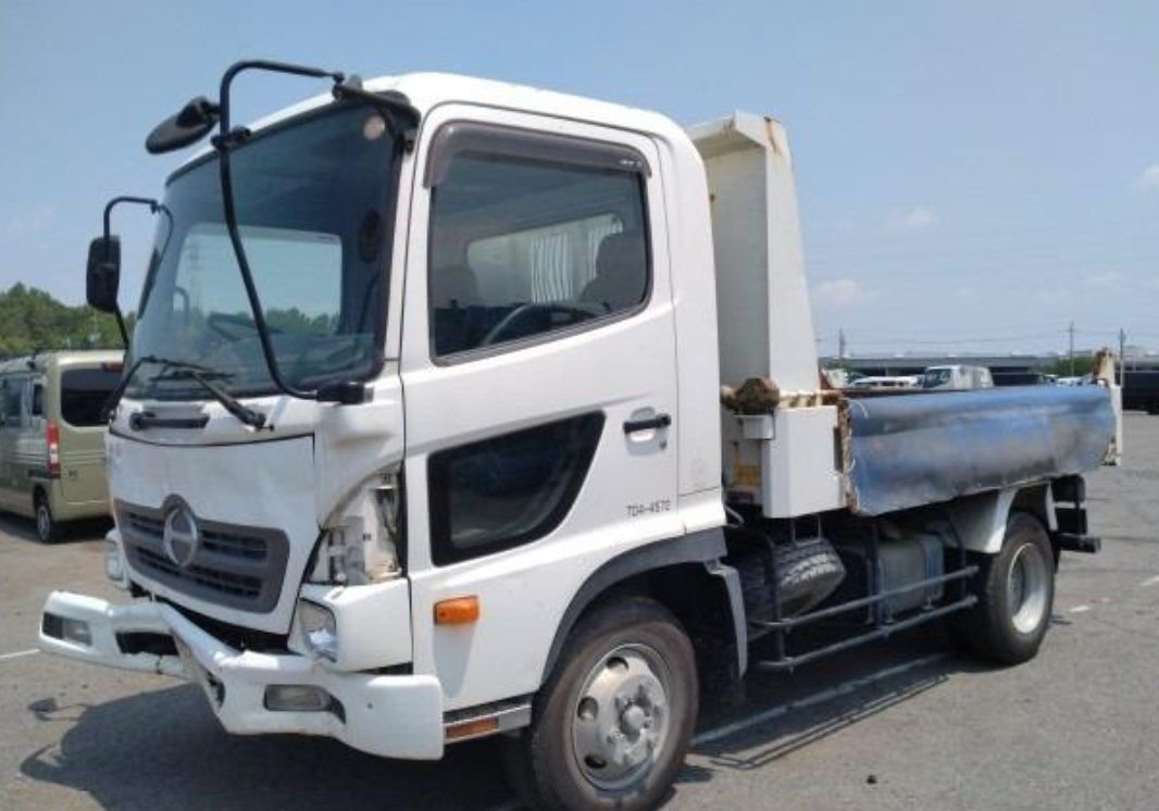 White Hino Ranger dump truck seen from the front left, showing the bent front bumper