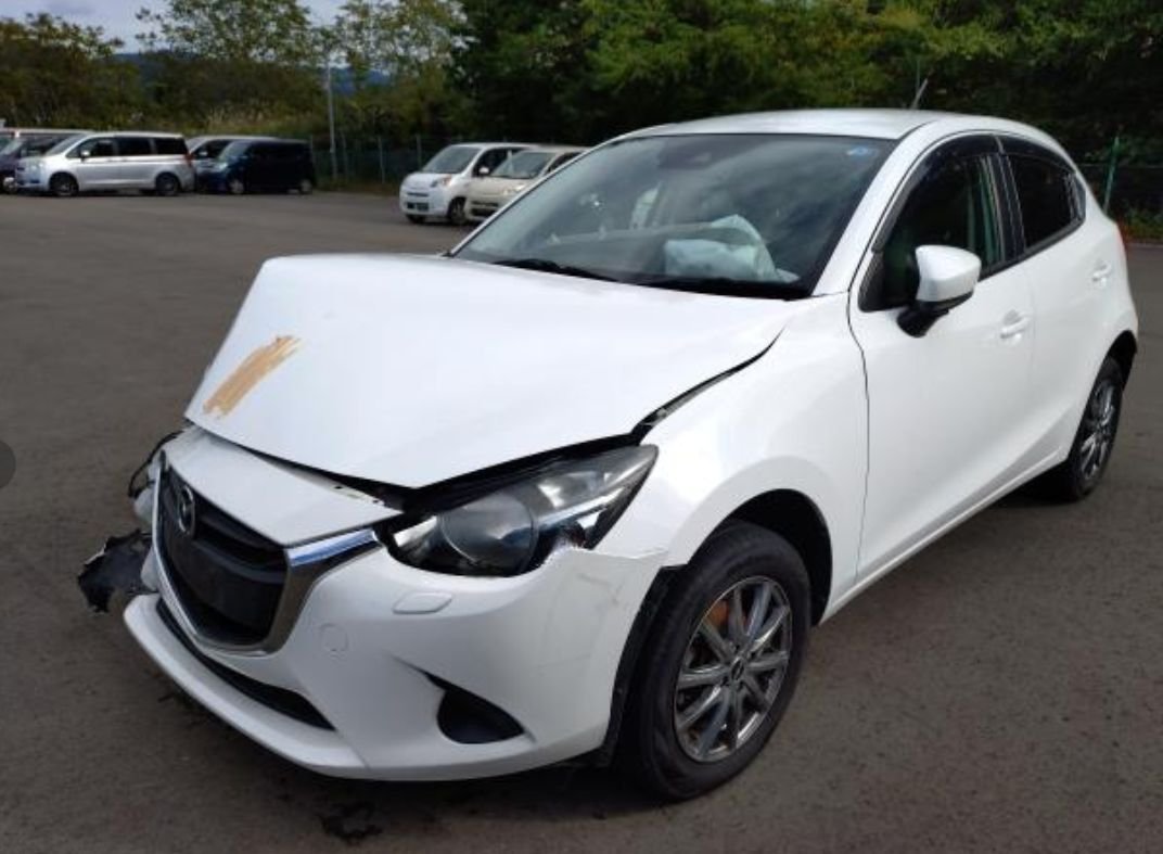 White Mazda Demio seen from the front left with a crumpled bonnet and front damage