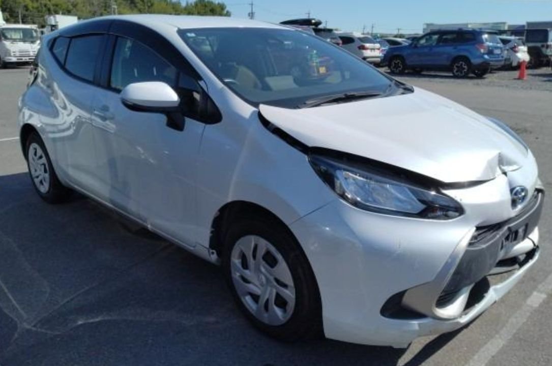 Pearl white Toyota Aqua seen from the front right with a dented bonnet and bumper