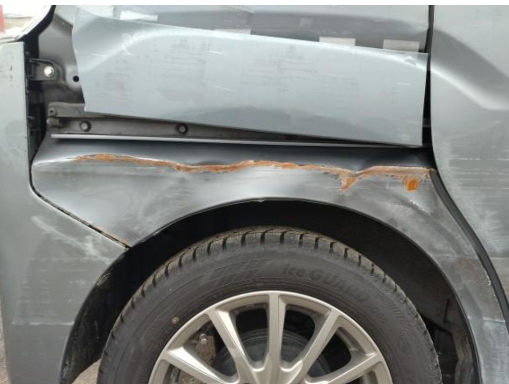Close-up of the scraped right rear panel and rusted wheel arch